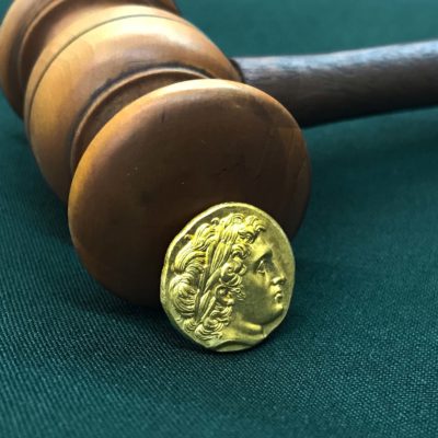 A gold Phillip II of Macedon Gold Stater with a gavel in the background.